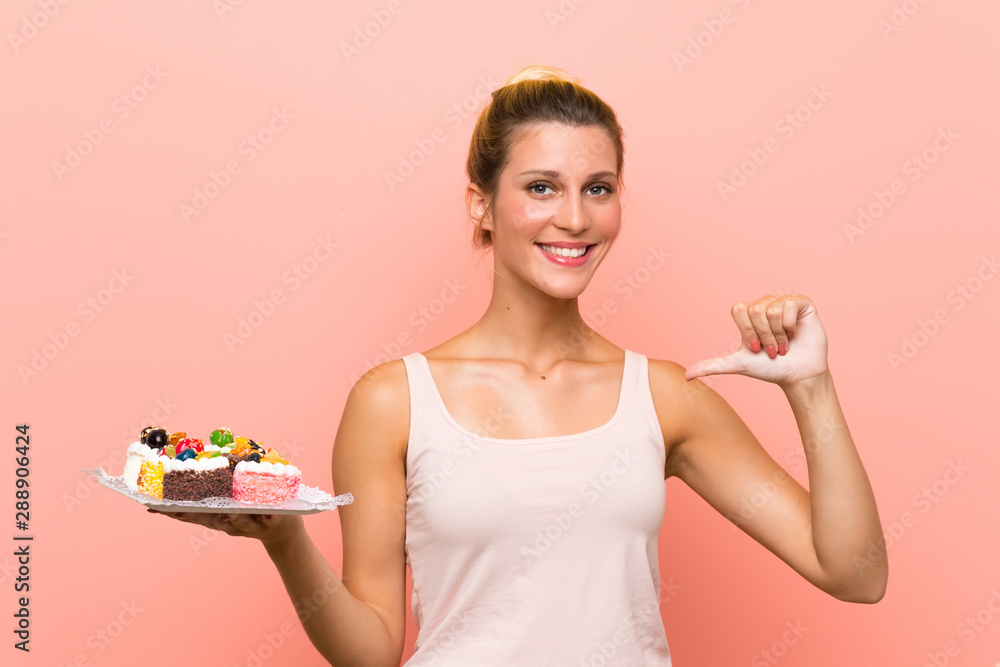 Young blonde woman holding lots of different mini cakes proud and self-satisfied Young blonde woman holding lots of different mini cakes proud and self-satisfied