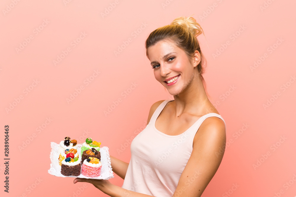 Young blonde woman holding lots of different mini cakes Young blonde woman holding lots of different mini cakes