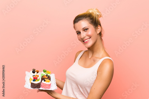 Young blonde woman holding lots of different mini cakes