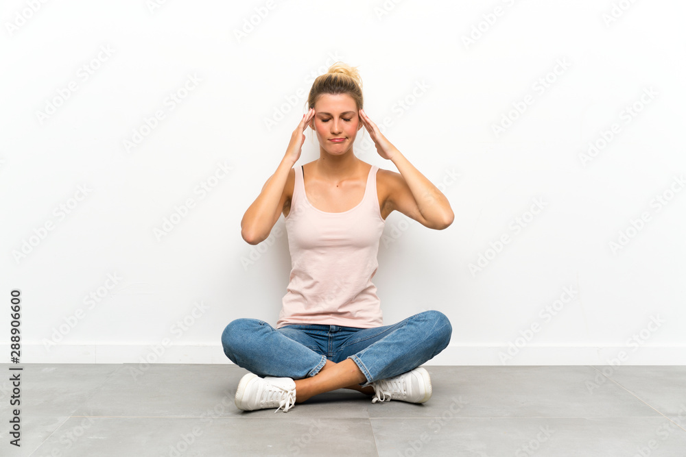 Young blonde woman sitting on the floor unhappy and frustrated with something. Negative facial expression Young blonde woman sitting on the floor unhappy and frustrated with something. Negative facial expression