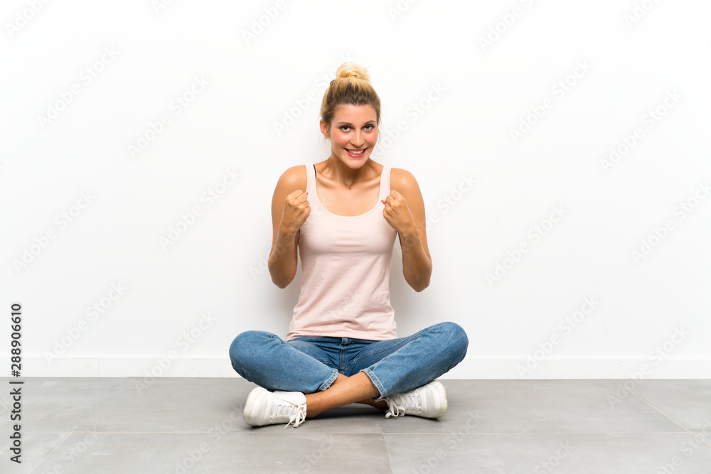 Young blonde woman sitting on the floor celebrating a victory Young blonde woman sitting on the floor celebrating a victory