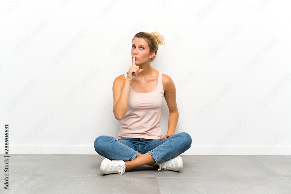 Young blonde woman sitting on the floor doing silence gesture