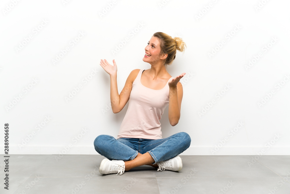 Young blonde woman sitting on the floor with surprise facial expression Young blonde woman sitting on the floor with surprise facial expression