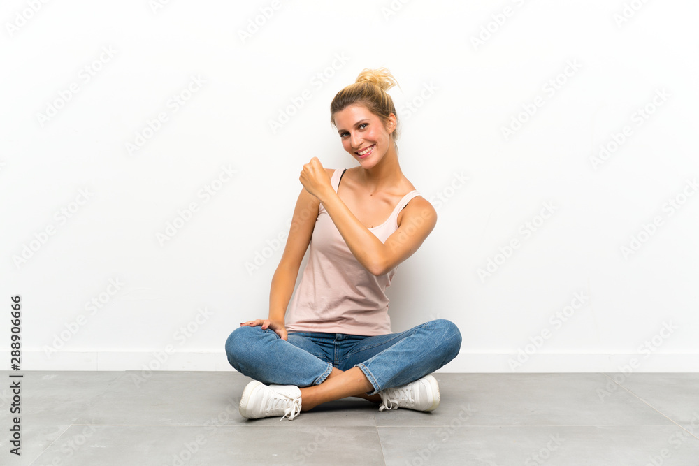 Young blonde woman sitting on the floor celebrating a victory