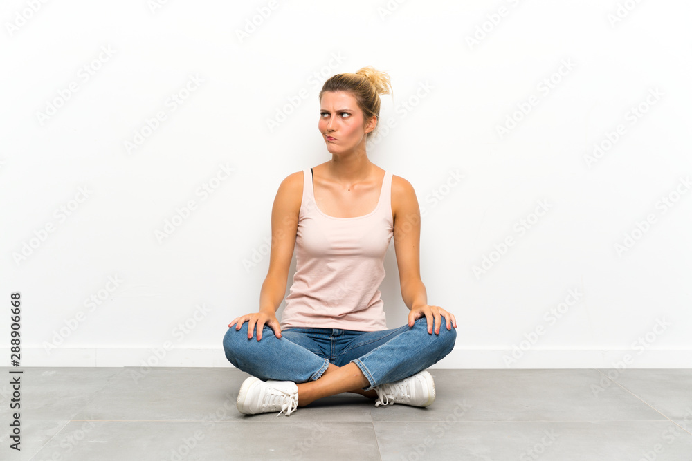 Young blonde woman sitting on the floor standing and looking to the side Young blonde woman sitting on the floor standing and looking to the side