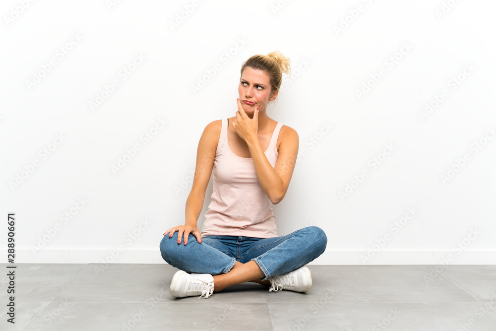 Young blonde woman sitting on the floor thinking an idea Young blonde woman sitting on the floor thinking an idea