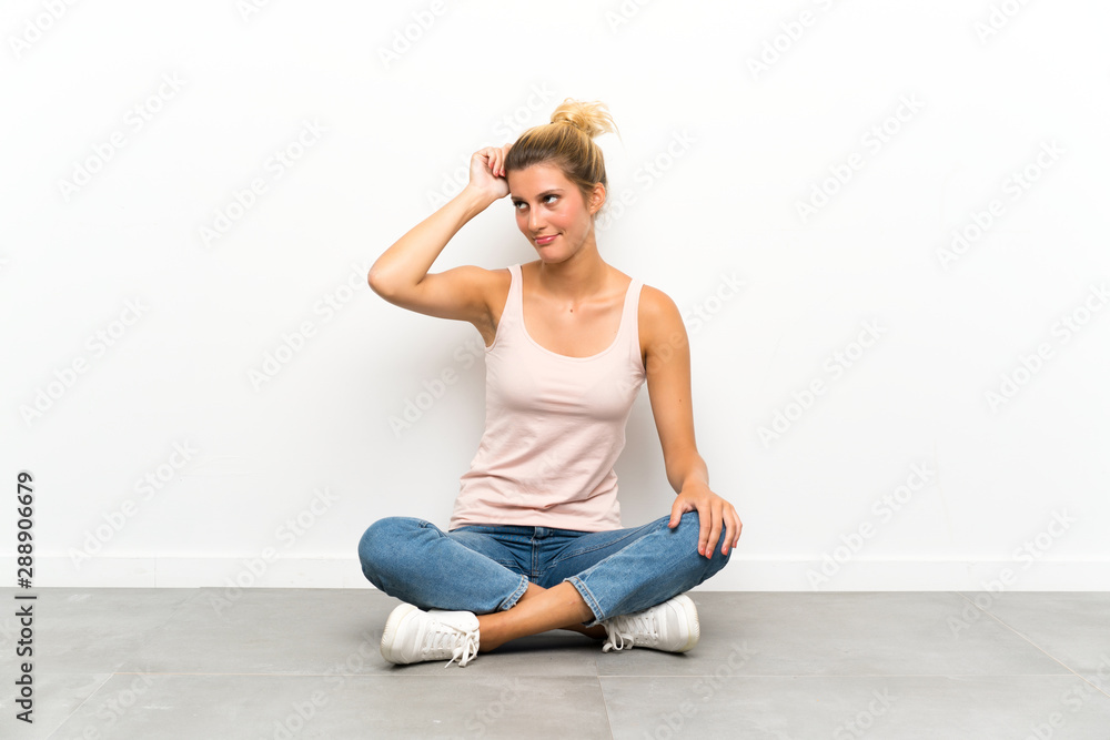 Young blonde woman sitting on the floor having doubts and with confuse face expression Young blonde woman sitting on the floor having doubts and with confuse face expression