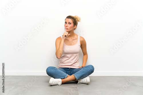 Young blonde woman sitting on the floor doing silence gesture