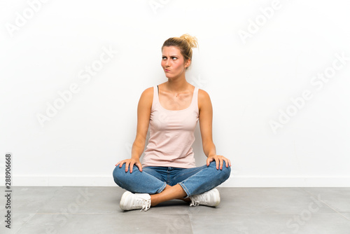Young blonde woman sitting on the floor standing and looking to the side