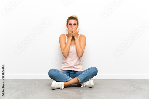 Young blonde woman sitting on the floor with surprise facial expression