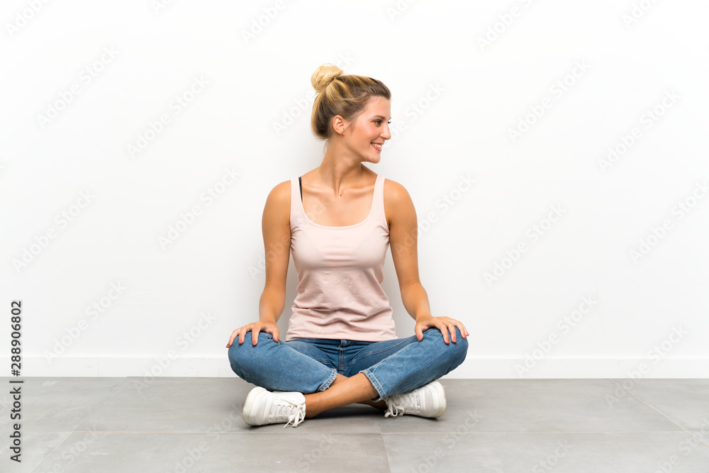 Young blonde woman sitting on the floor looking to the side