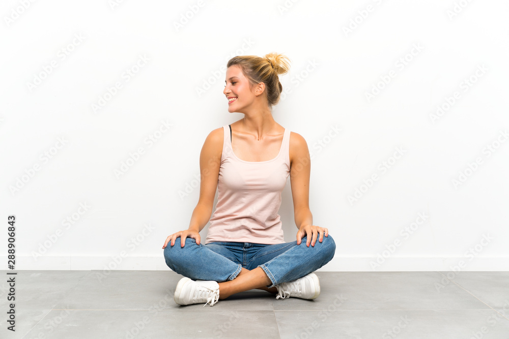Young blonde woman sitting on the floor laughing and looking up Young blonde woman sitting on the floor laughing and looking up