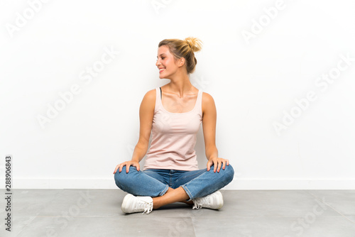 Young blonde woman sitting on the floor laughing and looking up