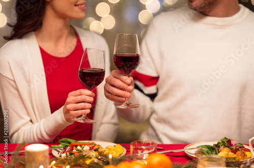 holidays, family and celebration concept - close up of happy couple having christmas dinner at home and drinking red wine
