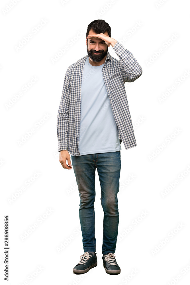 Handsome man with beard looking far away with hand to look something over isolated white background Handsome man with beard looking far away with hand to look something over isolated white background