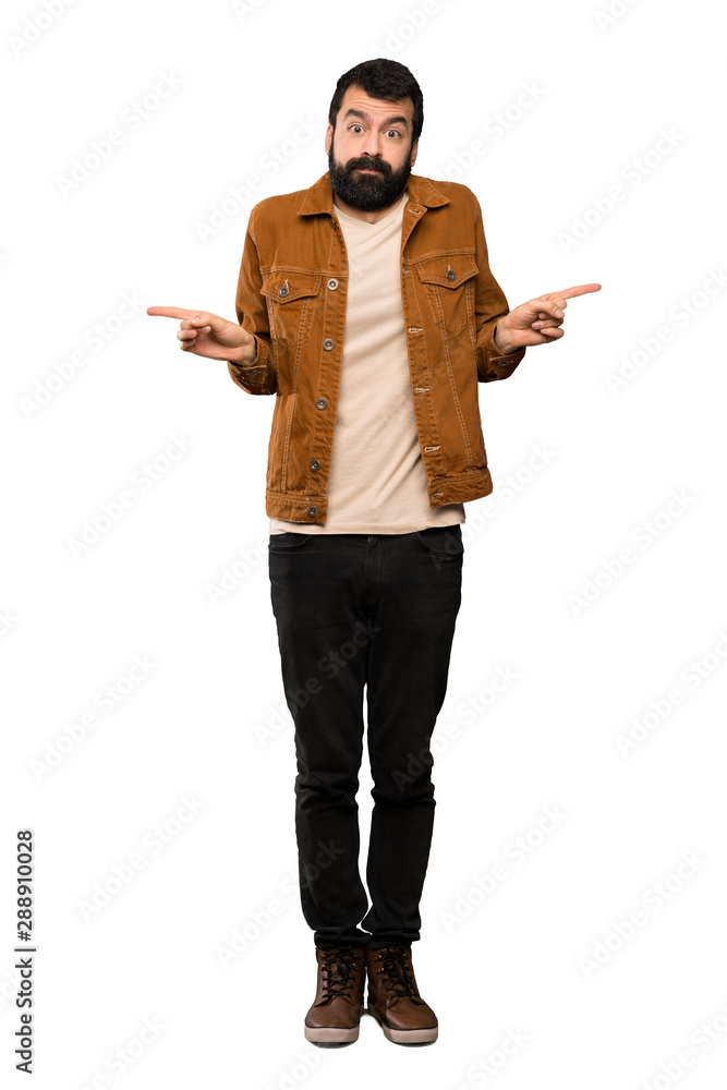 Handsome man with beard pointing to the laterals having doubts over isolated white background Handsome man with beard pointing to the laterals having doubts over isolated white background