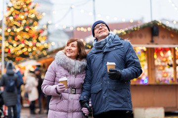 love, winter holidays and people concept - happy senior couple with takeaway coffee at christmas market on town hall square in tallinn, estonia
