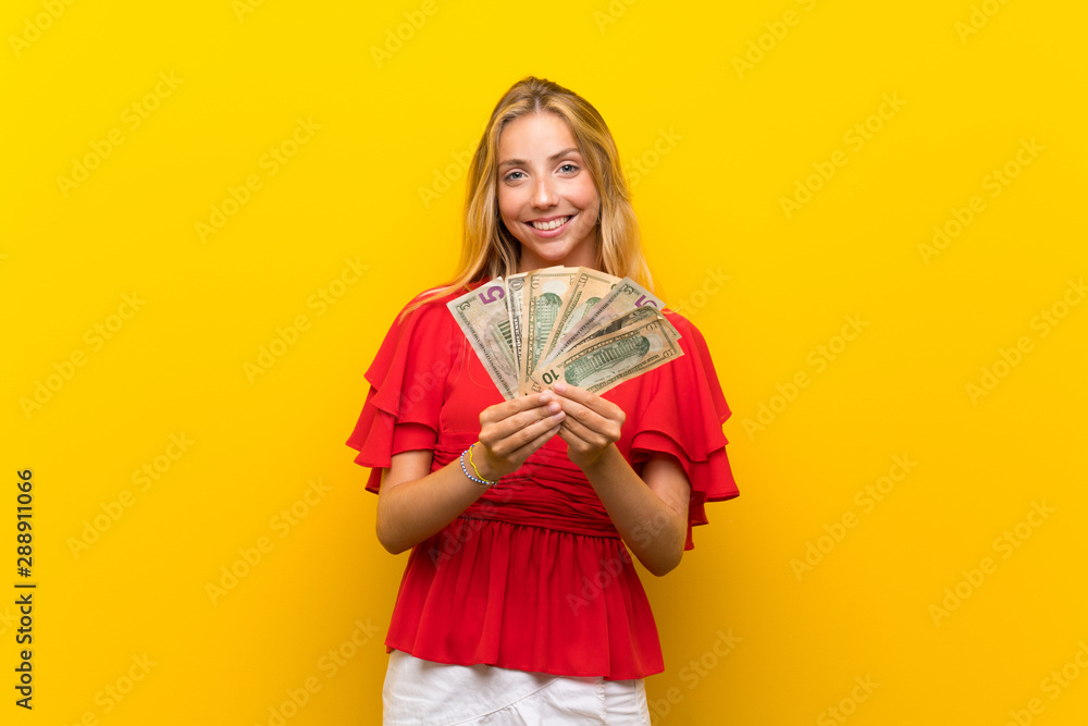 Blonde young woman over isolated yellow background taking a lot of money Blonde young woman over isolated yellow background taking a lot of money