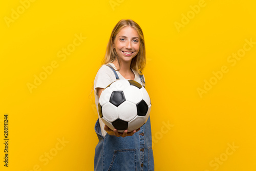 Blonde young woman over isolated yellow background holding a soccer ball © luismolinero