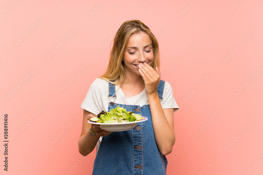 Blonde young woman with salad over isolated pink wall smiling a lot Blonde young woman with salad over isolated pink wall smiling a lot