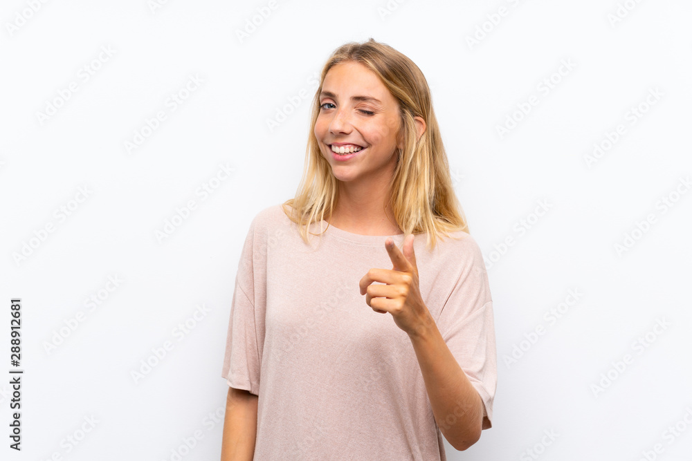 Blonde young woman over isolated white background points finger at you Blonde young woman over isolated white background points finger at you