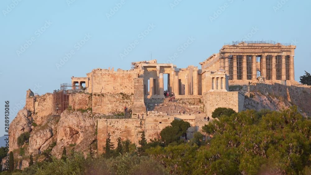 Tourists walking around the Acropolis of Athens. Icon of the hellenic civilization, Parthenon. Picturesque view of antique marble ruins on hill. Mediterranean plants near famous historical temple Tourists walking around the Acropolis of Athens. Icon of the hellenic civilization, Parthenon. Picturesque view of antique marble ruins on hill. Mediterranean plants near famous historical temple