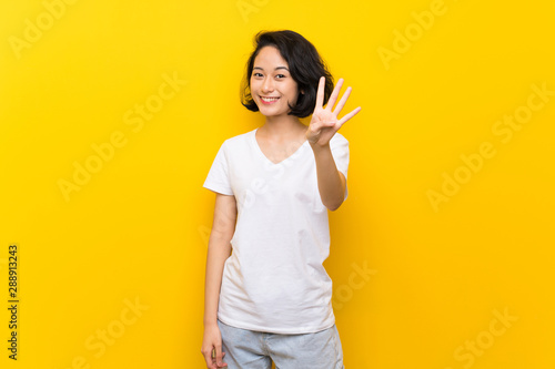 Asian young woman over isolated yellow wall happy and counting four with fingers