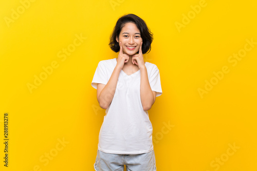 Asian young woman over isolated yellow wall smiling with a happy and pleasant expression