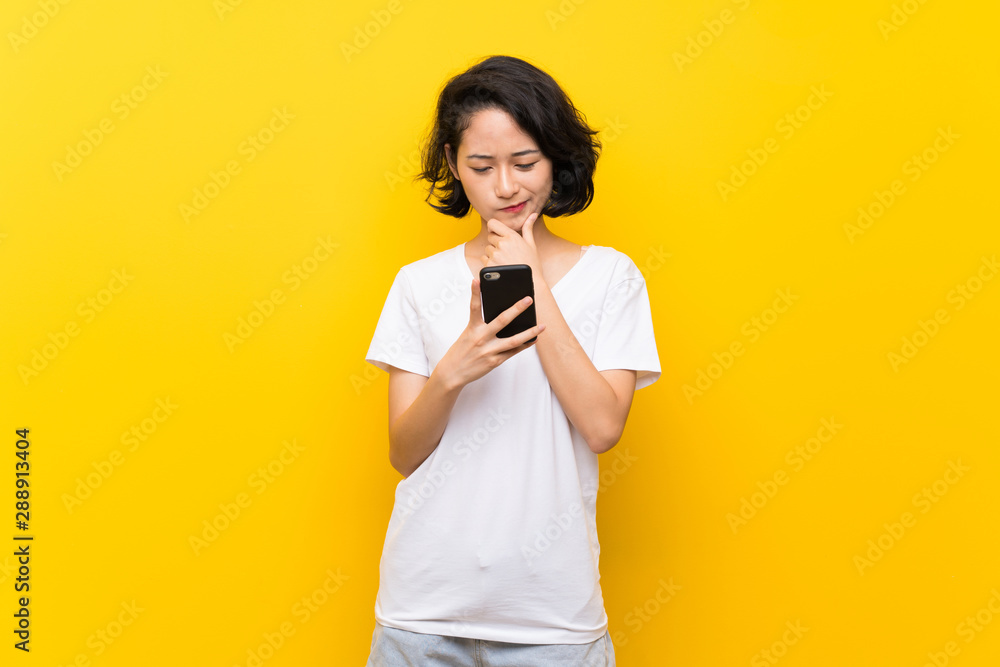 Asian young woman over isolated yellow wall thinking and sending a message Asian young woman over isolated yellow wall thinking and sending a message