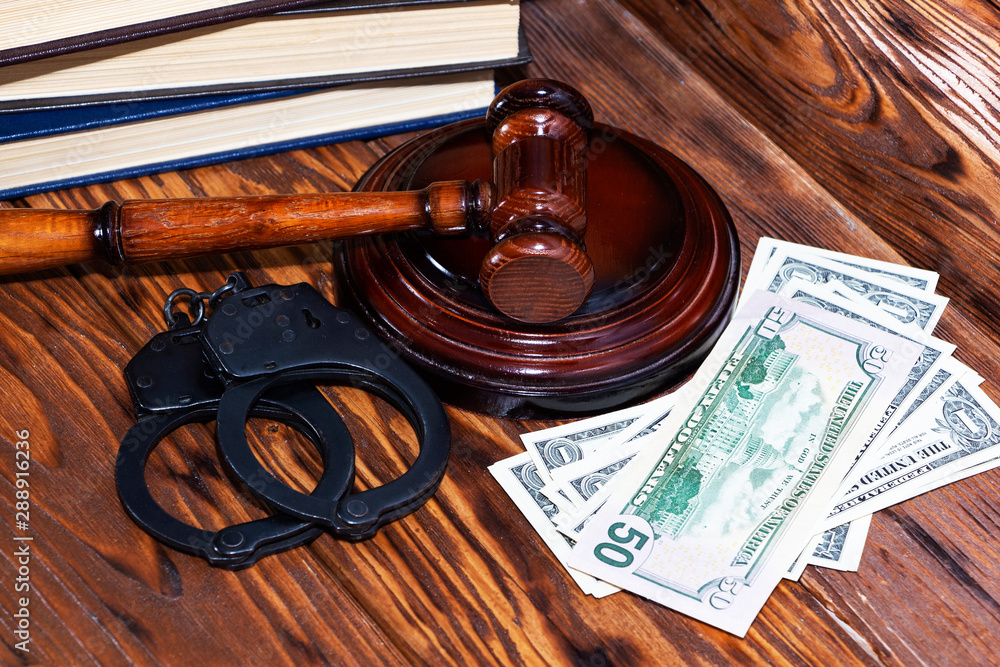 Judge's gavel with handcuffs on the background of dollar bills