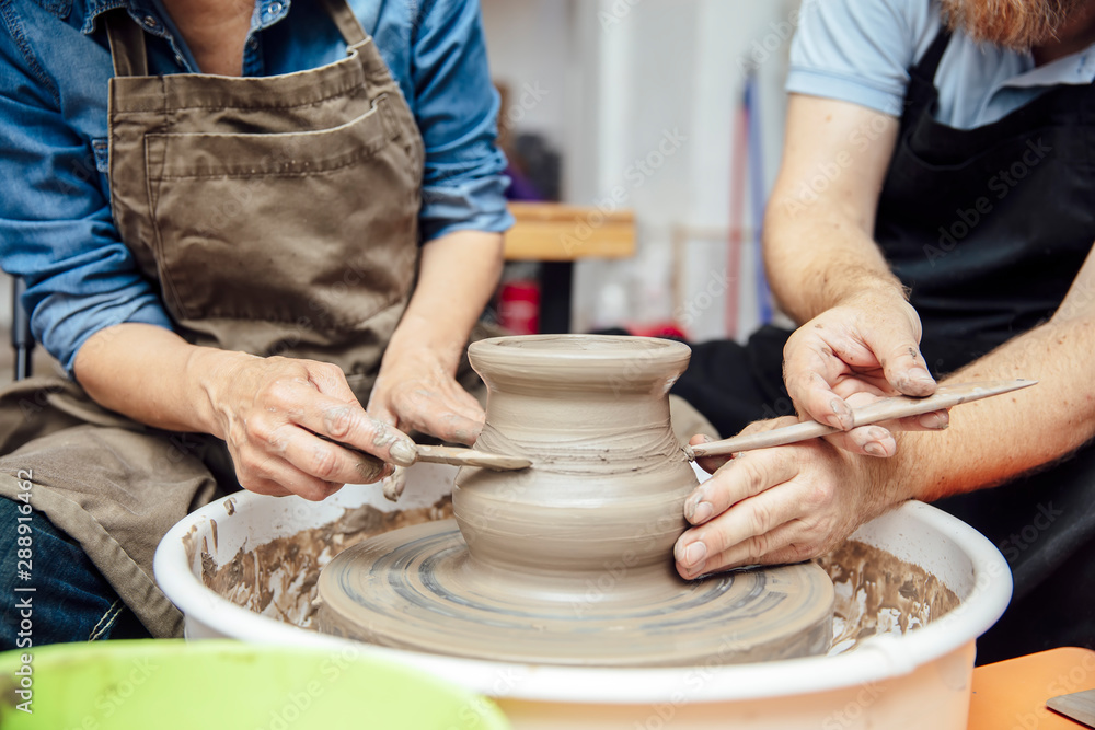 Senior woman spinning clay on a wheel with teacher at pottery class Senior woman spinning clay on a wheel with teacher at pottery class