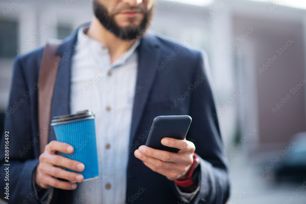 Bearded businessman reading e-mail on phone and holding coffee cup Bearded businessman reading e-mail on phone and holding coffee cup