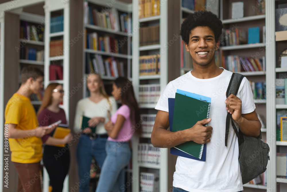 Excited african american student posing next to bookshelves in library - obrazy, fototapety, plakaty 