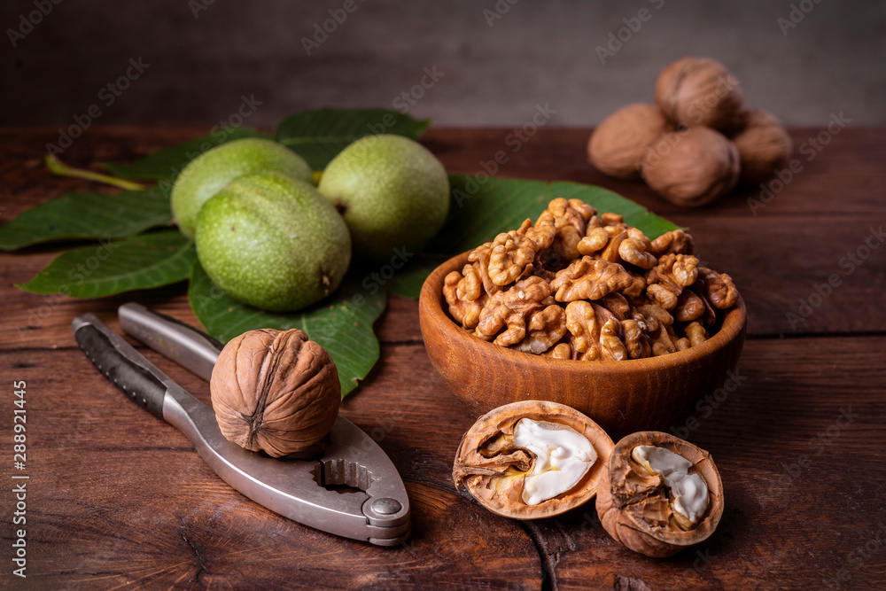 Walnuts chopped in a bowl, whole and in a green peel and a nut cracker on a dark old wooden background. Walnuts chopped in a bowl, whole and in a green peel and a nut cracker on a dark old wooden background.