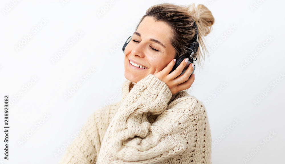 Beautiful European young woman in beige loose sweater, relaxing with closed eyes, smiling, listening to favourite songs via earphones, using music app. Pretty female enjoying different audio tracks Beautiful European young woman in beige loose sweater, relaxing with closed eyes, smiling, listening to favourite songs via earphones, using music app. Pretty female enjoying different audio tracks
