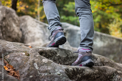 Woman is wearing hiking boot and walking on rocks in forest at autumn.