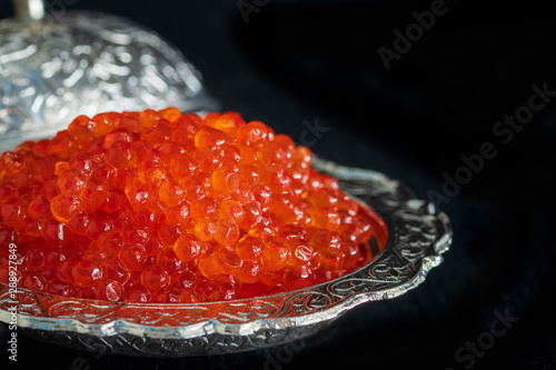 Red caviar in silver bowl on black background