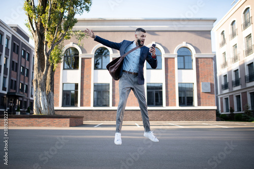 Businessman holding phone jumping while feeling emotional