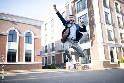 Man holding phone screaming and jumping after receiving good news