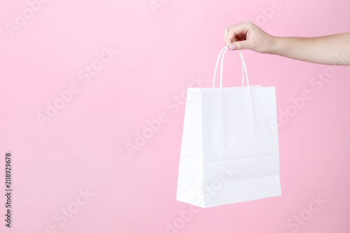 Female hand holding white shopping bag on pink background