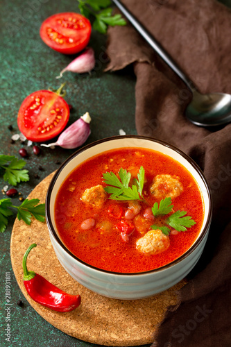 Tomato soup with meatballs and chili peppers on a dark stone or slate table. Top view flat lay.