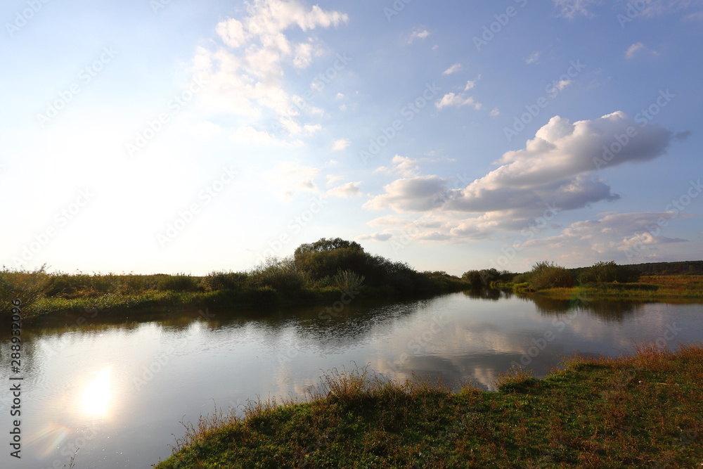 Summer rural landscape with small river, bright blue sky, white clouds reflect in the water. Have a nice summer day