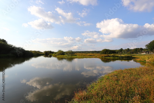 Summer rural landscape with small river, bright blue sky, white clouds reflect in the water. Have a nice summer day