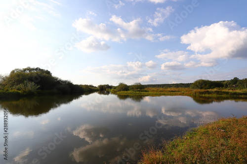 Summer rural landscape with small river  bright blue sky  white clouds reflect in the water. Have a nice summer day