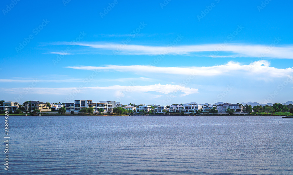 Wide panoramic view of Emerald Lakes residences across the lake, on a blue sky background during a beautiful sunset.