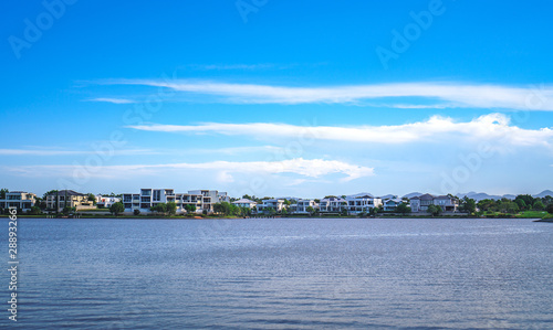 Wide panoramic view of Emerald Lakes residences across the lake, on a blue sky background during a beautiful sunset.