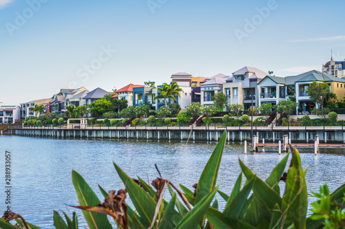  Wide panoramic view of Emerald Lakes residences across the lake, on a blue sky background during a beautiful sunset. Gold Coast, Australia.