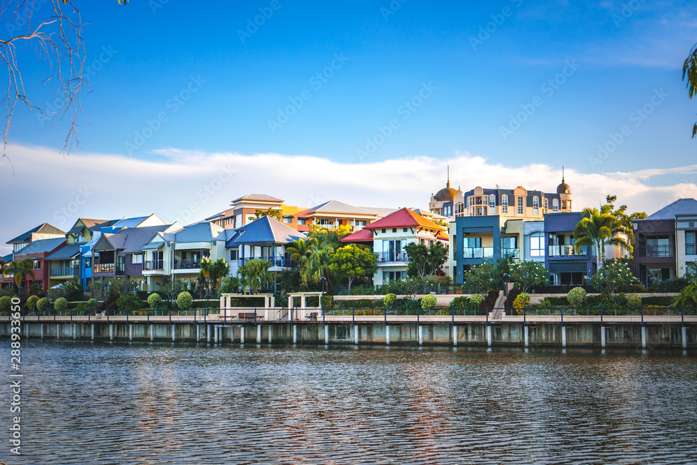  Wide panoramic view of Emerald Lakes residences across the lake, on a blue sky background during a beautiful sunset. Gold Coast, Australia.