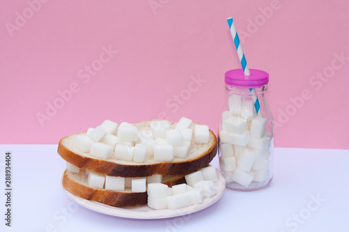 Sandwich with sugar and bottle full of sugar cubes. Too much sugar and unhealthy food concept.