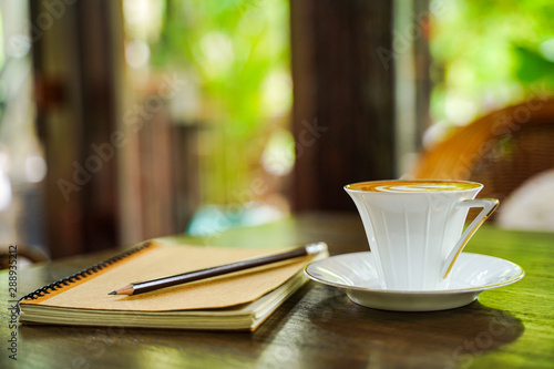 white ceramic coffee cup on wooden tablewith brown notebook and pencil